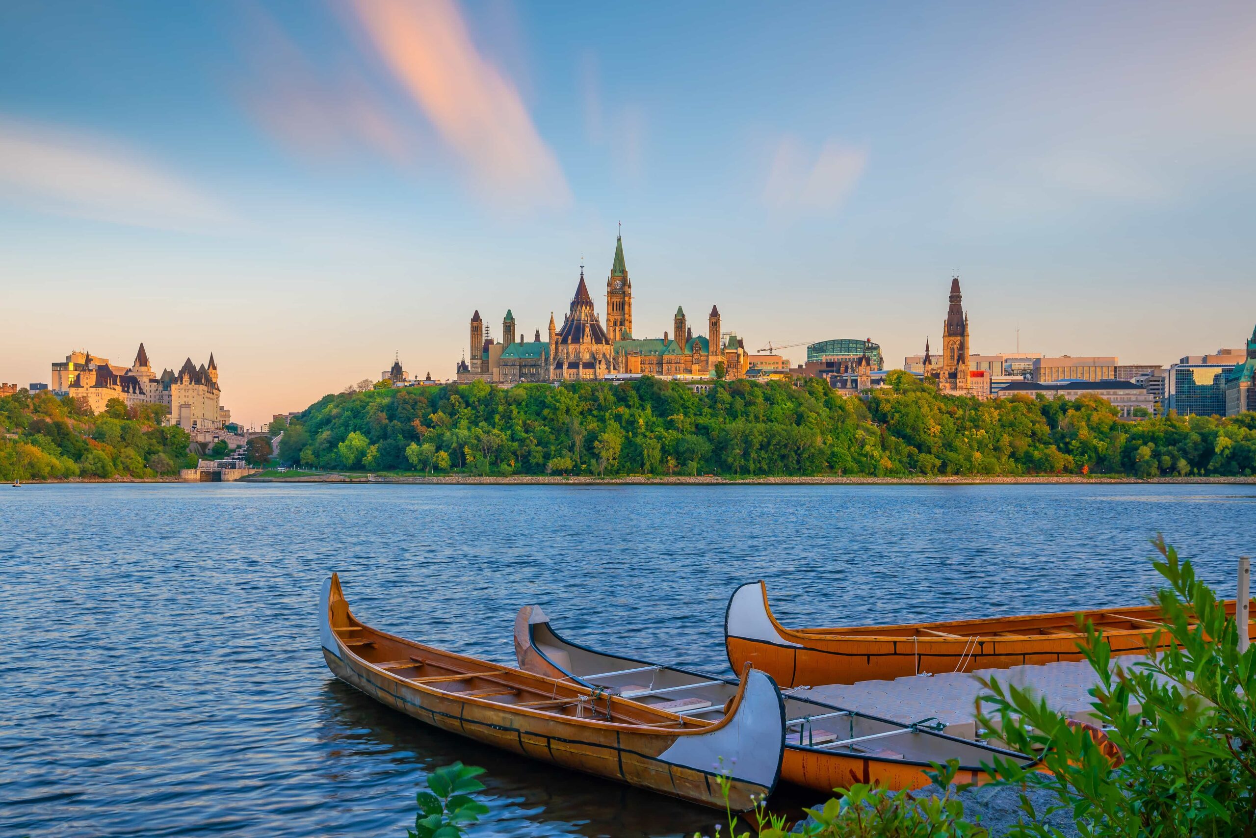 Two wooden canoes on a river with Parliament Hill and historic buildings in Ottawa, Canada, in the background at sunset.
